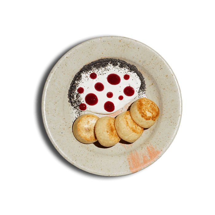 Тарілка золотистих сирників зі сметаною — традиційна українська страва від ресторану 100 років тому вперед.